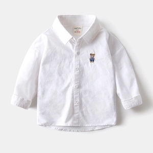 Détail d'une chemise blanche en coton pour garçon avec petite broderie d'ours et boutons