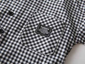 Detail of boys' gingham shirt featuring a chest pocket with fashion slogan textile label