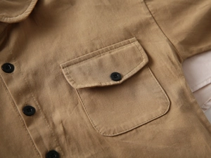 Détail d'une chemise en coton kaki avec poche à rabat et bouton noir contrastant