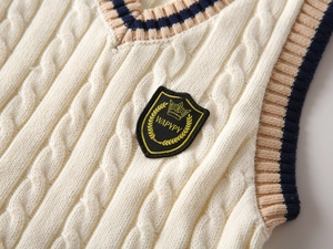 Detailed macro view of cable knit texture and embroidered shield badge on ivory sweater vest