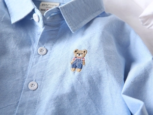 Détail d'une chemise Oxford bleu clair pour garçon avec broderie ours et texture du tissu