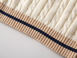 Close-up of cable knit texture and striped ribbed hem on a cream children sweater