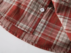 Close-up of red plaid cotton shirt hem with white resin button and neat stitching