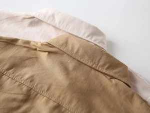 Gros plan de chemises enfant empilées rose et kaki montrant le col et la texture du coton
