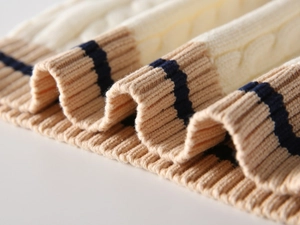 Detailed macro view of cream knitted sweater with navy stripe ribbing and cable texture