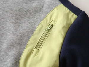 Détail d'une veste bicolore avec tissu gris et poche à fermeture éclair verticale vert néon
