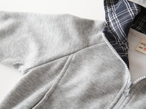 Nahaufnahme von grauem Kinder-Kapuzenpulli mit blau-kariertem Futter und Etikett