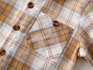 Macro detail of yellow and purple plaid shirt with textured brown button and pocket