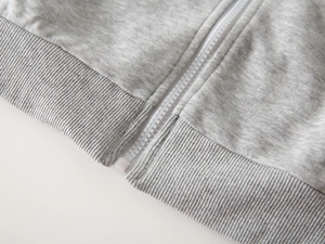 Detailansicht der grauen Jungen-Sweatjacke mit weißem Reißverschluss und Rippstrickbündchen