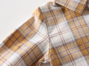 Detailed close-up showing texture of yellow plaid cotton shirt fabric and stitching quality