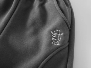 Détail d'un pantalon en maille gris foncé avec broderie chien blanc et texte 'cool' brodé