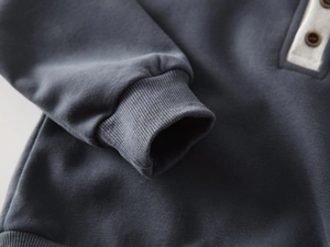 Macro shot of charcoal grey knitted fabric with ribbed cuffs and wooden button detail