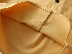 Detailed macro view of yellow cotton shirt hem sewing with neat stitching and button