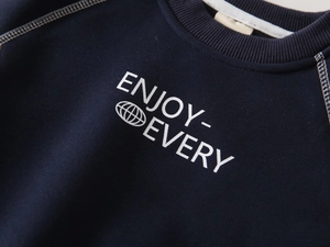 Detail of navy boy's sweatshirt with white stitching and ENJOY print on chest