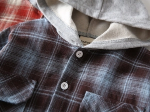 Detail des blau-braun karierten Hemdstoffs mit weißen Knöpfen und grauer Strickkapuze