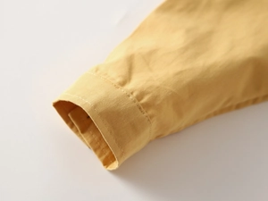Detailed close-up of yellow long-sleeved boy shirt cuff with neat stitching and cotton texture