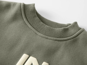 Detail of olive green sweatshirt showing ribbed crew neck and white IN textured print