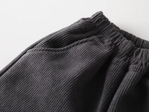 Detail of dark grey corduroy kids' trousers featuring elastic waistband and side pockets