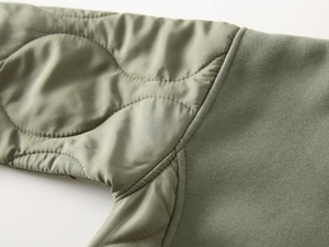 Detail of army green patchwork hoodie showing quilted nylon fabric and smooth stitching