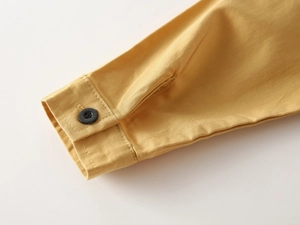 Detail of ginger yellow boy's cotton shirt sleeve with neat stitching and black button