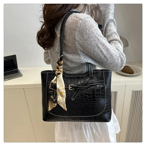 Detail of black crocodile pattern tote bag with decorative scarf and metal buckle