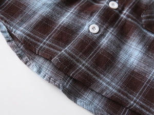 Detail der braun karierten Flanellstoff-Textur mit weißem Knopf und Rundsaum