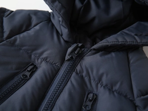 Detail of navy hooded winter coat featuring quilted fabric and dual chest zipper pockets