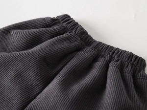 Detail of dark grey corduroy pants featuring an elastic waist and thick textured fabric