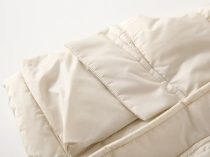 Macro view of cream quilted hooded vest featuring detailed stitching and pocket flap