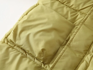 Close-up of mustard yellow quilted winter coat showing pocket stitching and nylon fabric