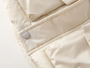 Detail of off-white quilted children's vest showing metal snap button and fine stitching