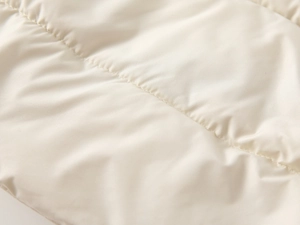 Detailed macro view of ivory padded jacket fabric with horizontal quilted stitching
