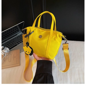 Detail of bright yellow nylon tote bag with wide strap and a black animal charm