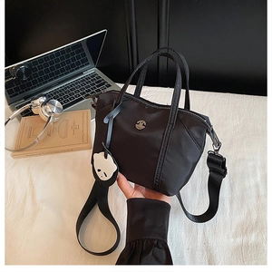 Detail of black nylon mini tote bag with panda pendant and adjustable strap on a desk