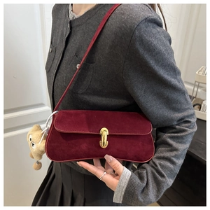 Détail du sac bandoulière en daim bordeaux avec boucle dorée et breloque ours en peluche