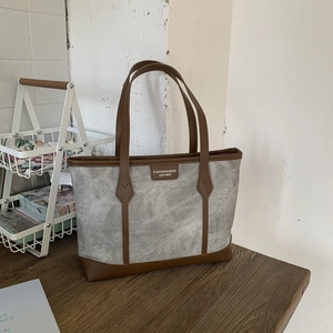Detail of grey canvas tote bag with brown leather trim and fashion leather patch label