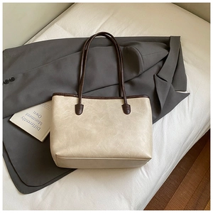 Close-up of beige leather tote bag with dark brown straps on white bedding