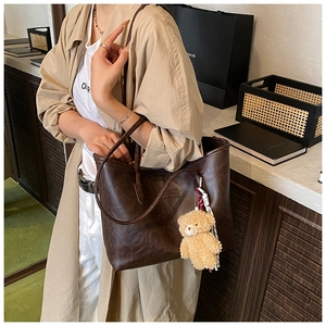 Detail of a large brown vintage tote bag with plush bear charm on a female model