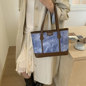 Blue denim tote bag with brown leather trim carried by model in a minimalist setting