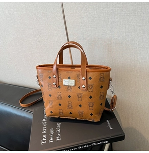 Détail du sac seau marron vintage avec motif ours et plaque logo posé sur des livres