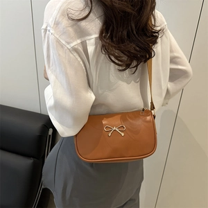 Brown minimalist shoulder bag with golden bow ornament on a neutral background