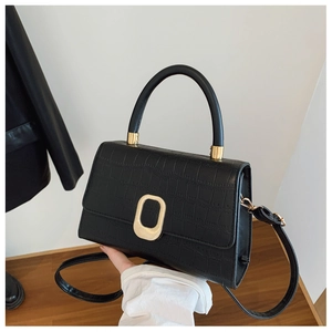 Detail of black crocodile texture handbag featuring a gold buckle and sturdy handle