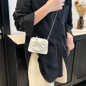 White mini chain bag with pearl handle and bow detail worn by model for crossbody style