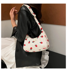 Close-up of white corduroy shoulder bag with red strawberry prints and metal buckles