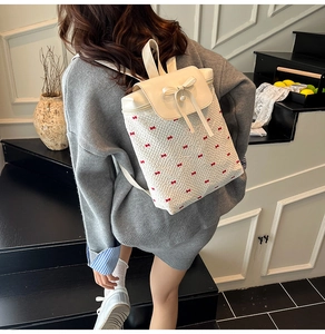 Detail of white lace backpack featuring red bow prints and a large pearl bow ornament