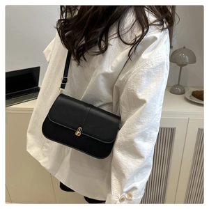 Detail of minimalist black baguette bag with gold metal buckle on a white shirt