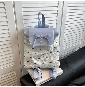 Close-up of lace backpack featuring light blue leather flap with bow and pearl charms