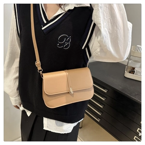 Khaki leather baguette bag with metal buckle and shoulder strap worn over a black vest