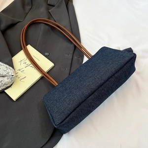 Detailed view of dark blue denim underarm bag with slim brown leather shoulder straps