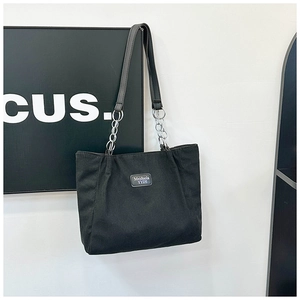 Detail of black corduroy tote bag featuring silver chain strap and square brand patch